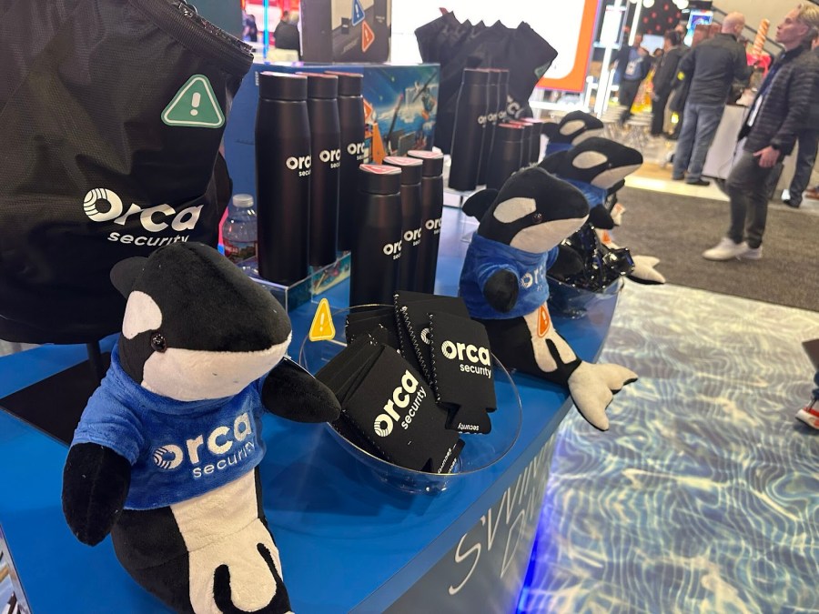 Orca Security branded swag including orca stuffed animals, koozies, water bottles, and tote bags