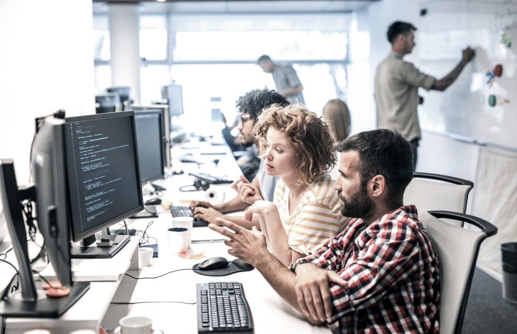 A stock photograph of colleagues looking at complex code on a workstation