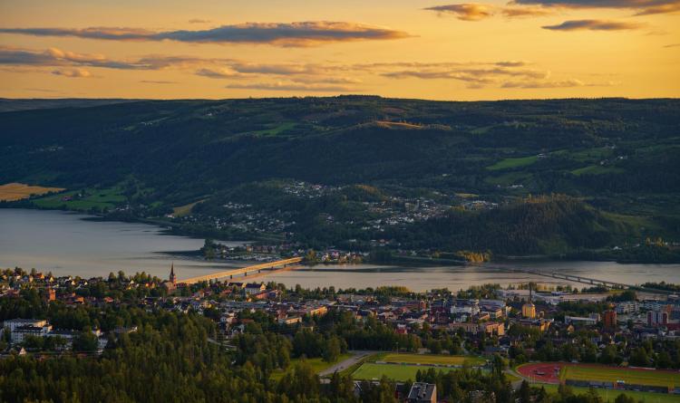 Aerial view of Lillehammer, Norway, during a summer sunset, with Lake Mjosa and surrounding hills in the background.