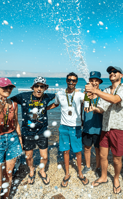 An image of Orca colleagues celebrating by popping champagne on the beach