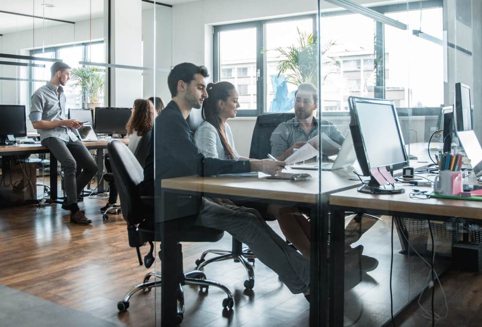 A photo of work colleagues collaborating together near their workstations