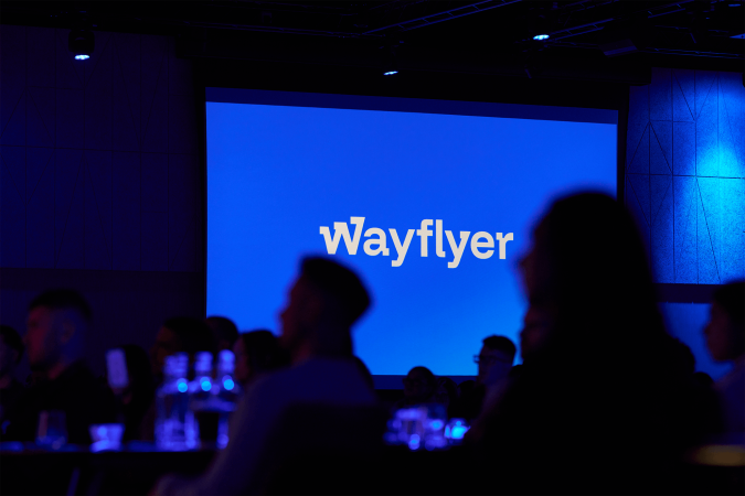 A photo of the Wayflyer logo on a projector screen during a conference